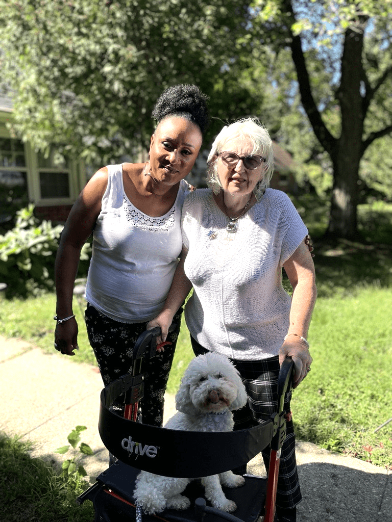 2 woman stand outside with a small white dog.