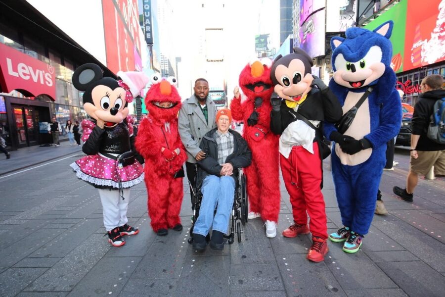 Times Square in NYC. Two men pose with people dressed up as characters like Minnie Mouse.