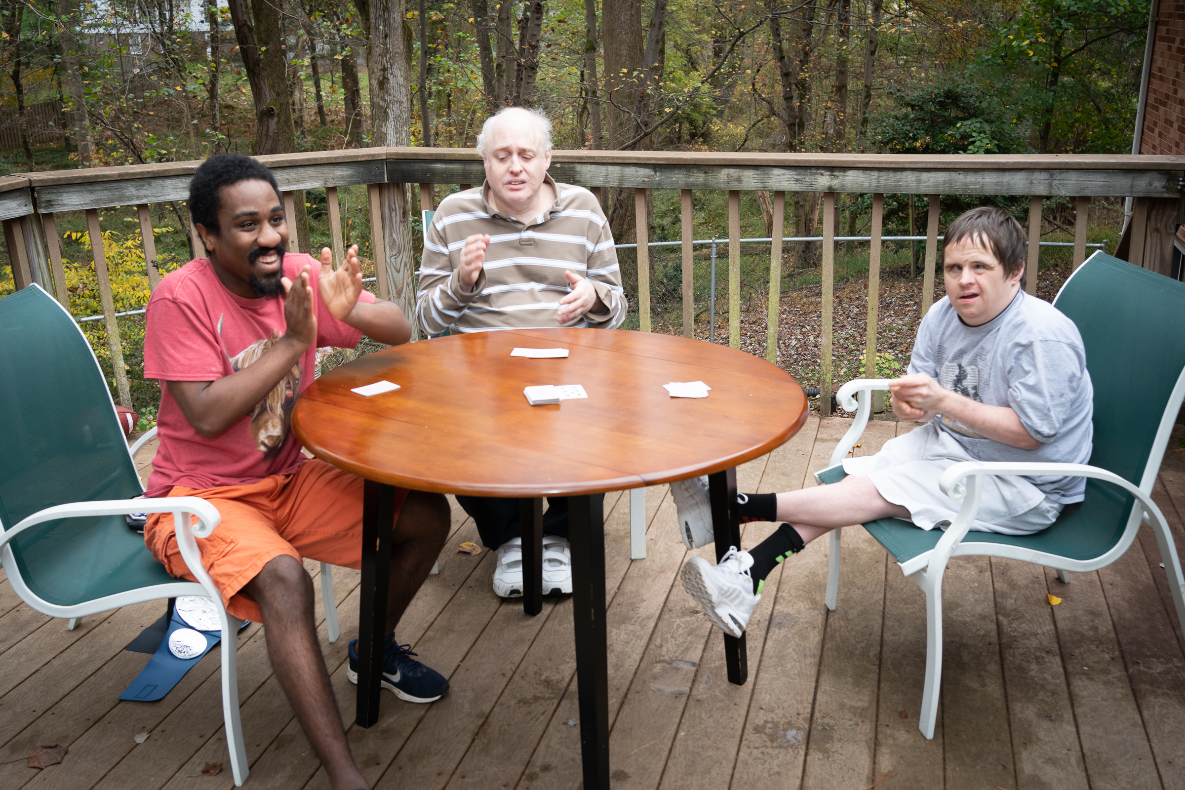 Three men at a table playing cards on an outdoor deck