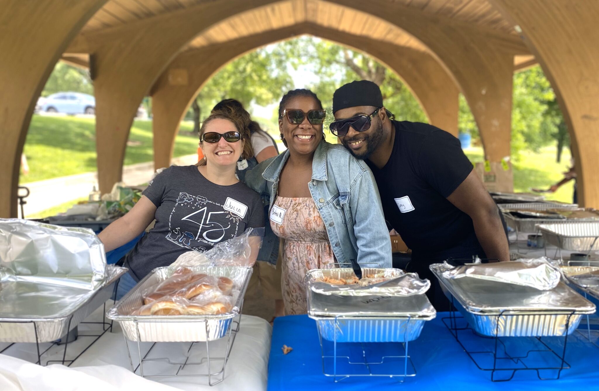 Three people serving food at an outdoor pavilion.