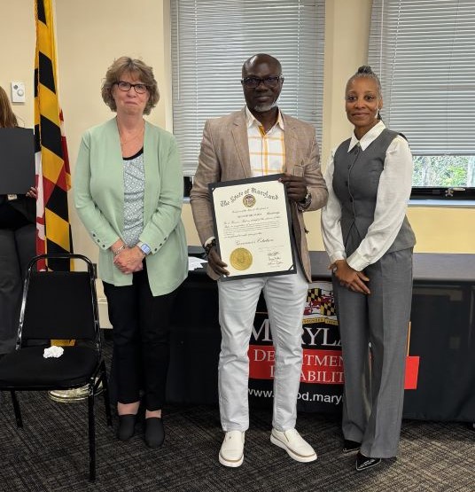 Femi Okunlola center holds an award certificate flanked by CAROL A. BEATTY, Secretary of Disabilities on the right and Marlana Hutchinson, Deputy Secretary DDA.