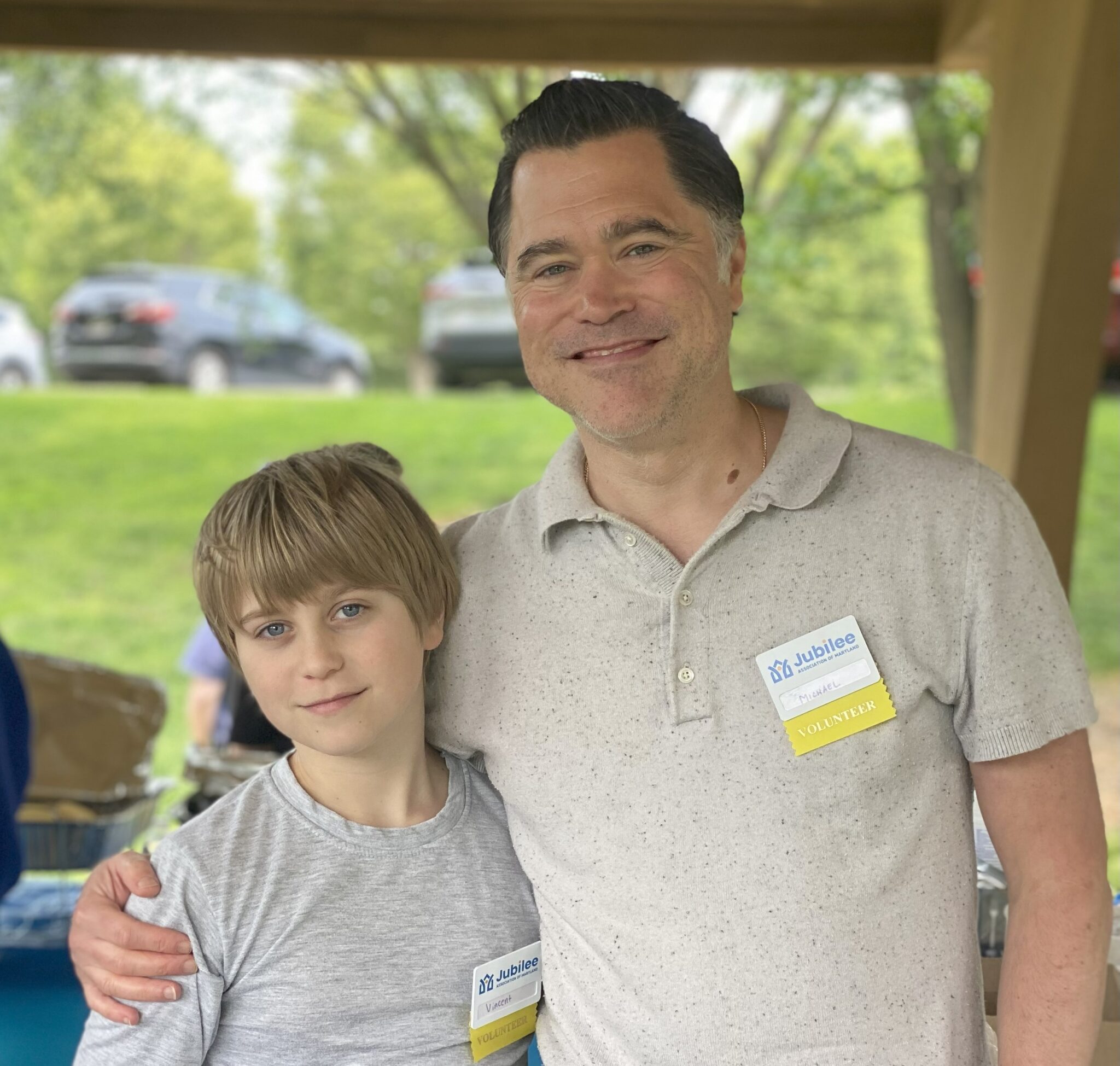 A man and young boy (father and son) at a cookout wearing volunteer name tags.