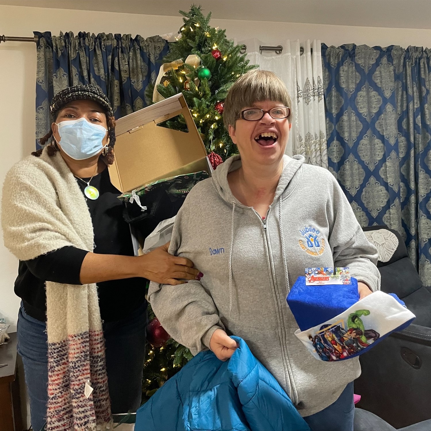 Two women open gifts in front of a Christmas tree
