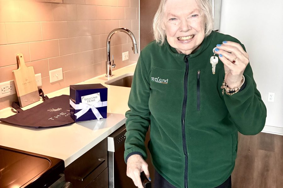 A woman smiles and holds up the keys to her new apartment