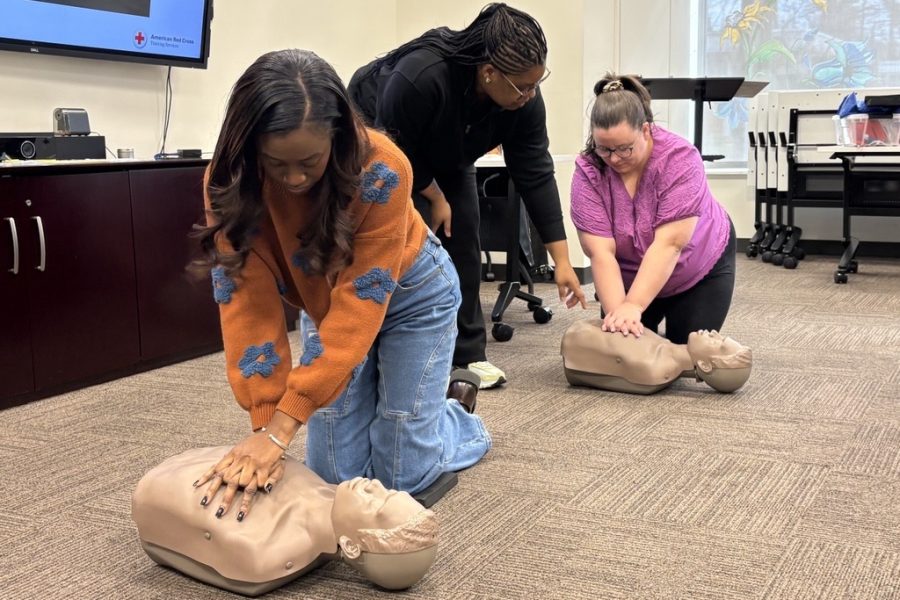 Two women practice with CPR dummies while an instructor provides advice