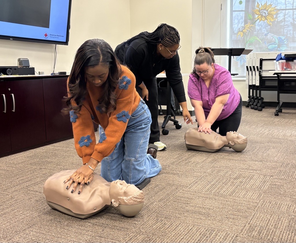 Two women practice with CPR dummies while an instructor provides advice