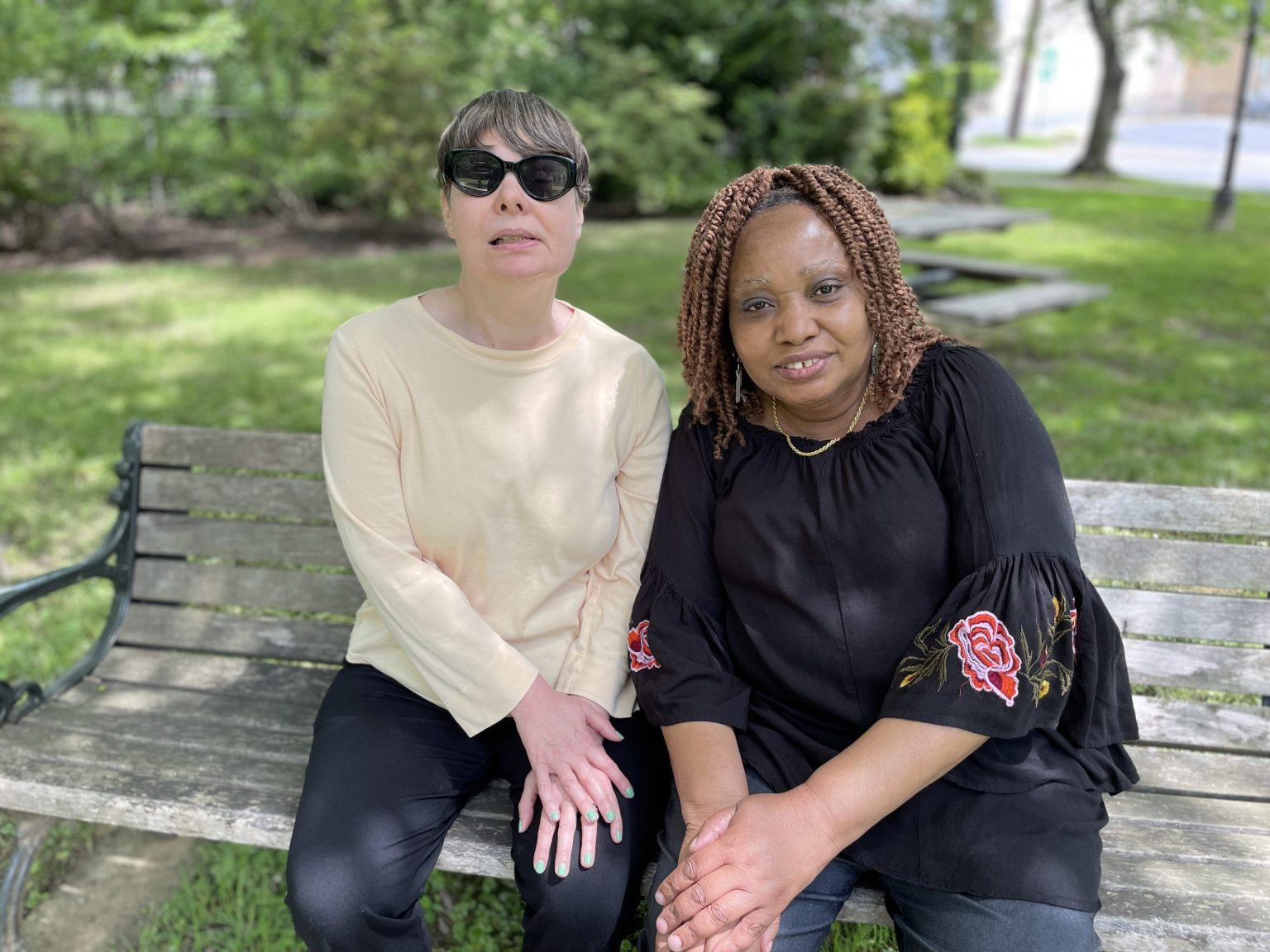 Two women sit on an outdoor bench together