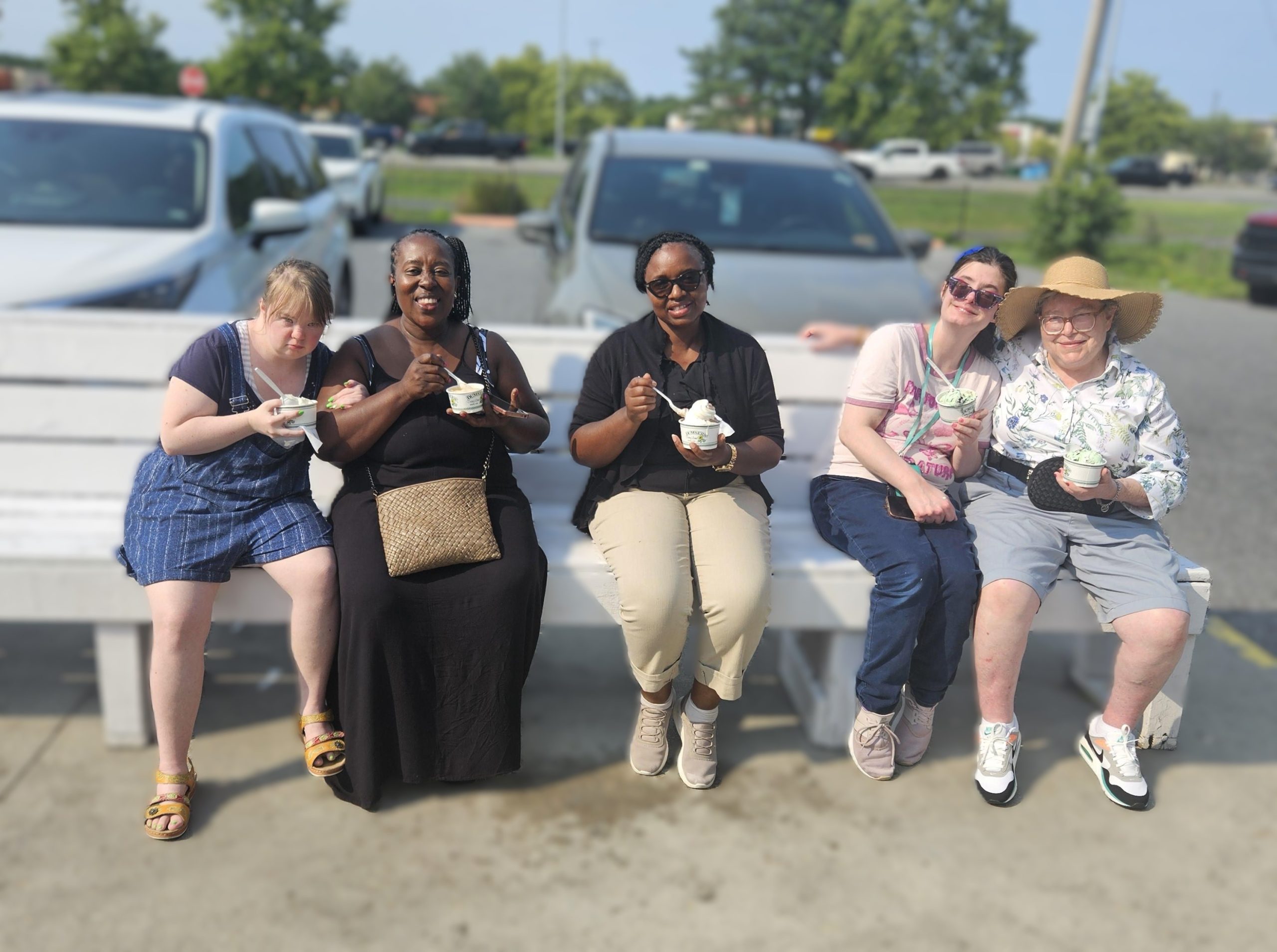 A group of friends eat ice cream on an outdoor bench on a hot summer day