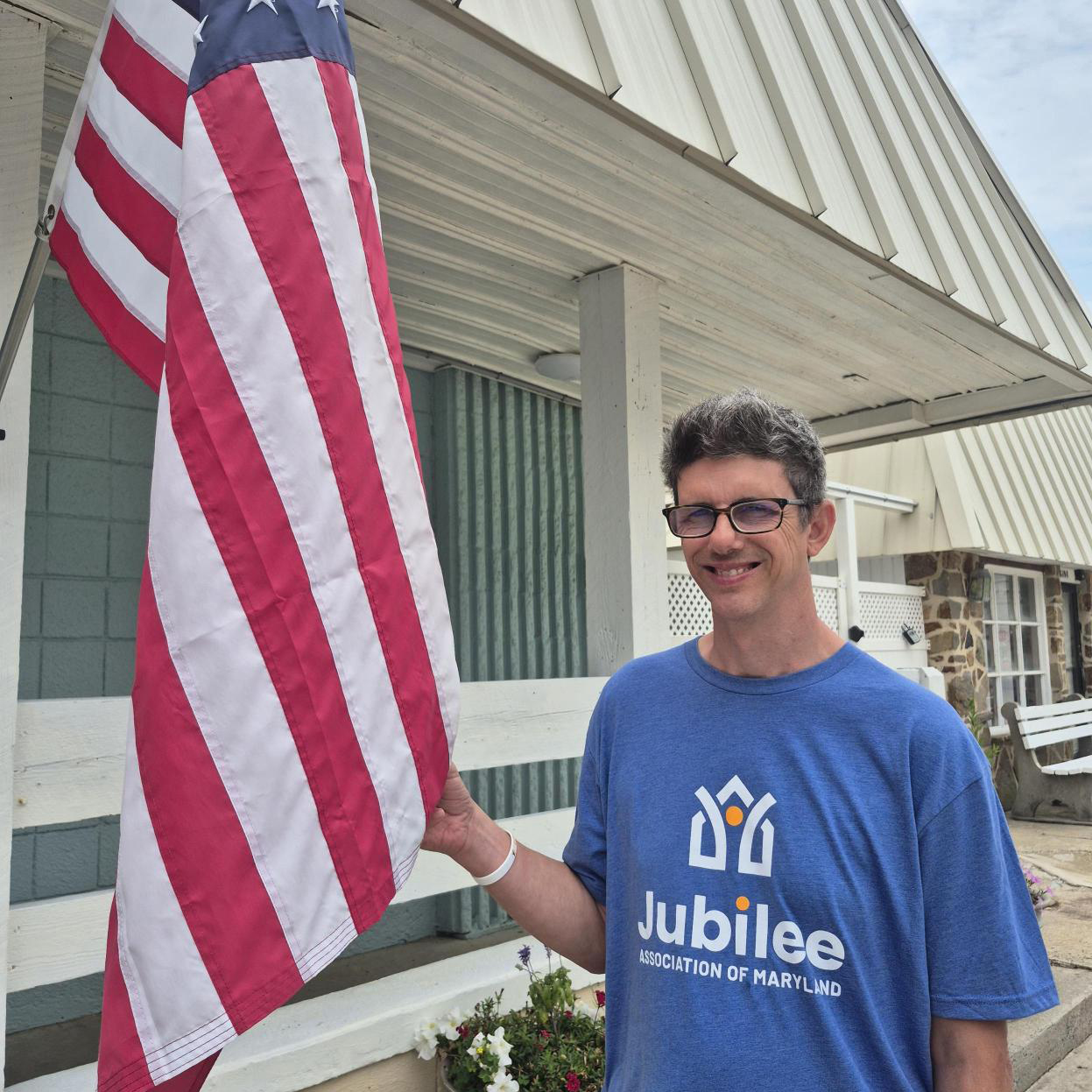 A man in a Jubilee t-shirt next to an American flag. Javi Requejo on vacation in Ocean City with Jubilee.