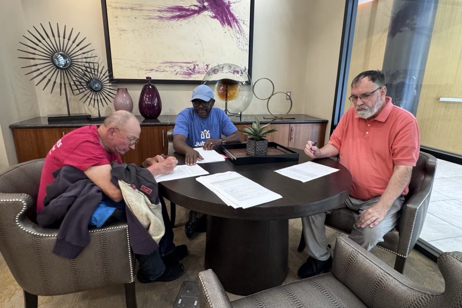 Two men sign a lease for their apartment while Jubilee support staff assist.